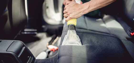 Person cleaning a cloth car seat with a brush and spray bottle